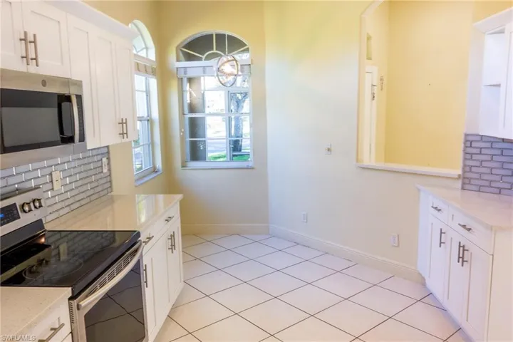 Kitchen featuring tasteful backsplash, stainless steel appliances, white cabinets, and light stone countertops