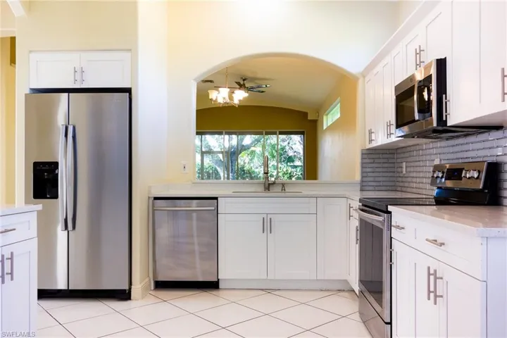 Kitchen with appliances with stainless steel finishes, white cabinets, light stone countertops, a chandelier, and backsplash