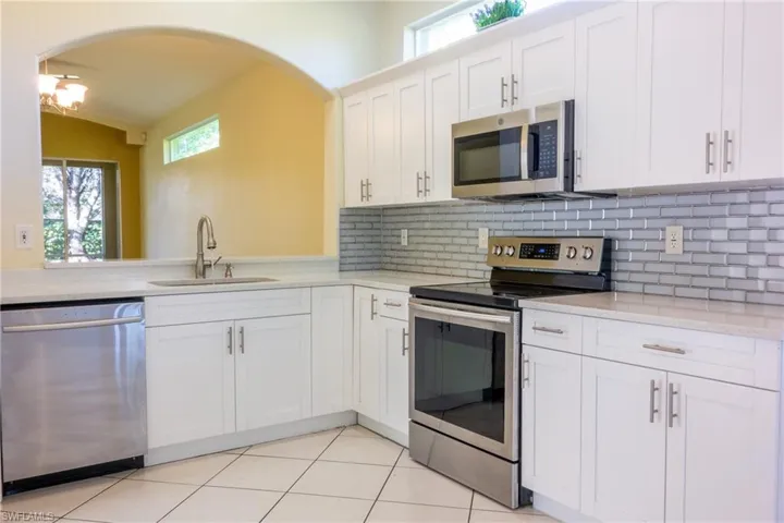 Kitchen featuring stainless steel appliances, plenty of natural light, white cabinetry, and light stone countertops