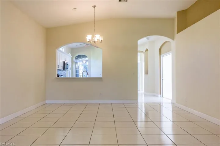 Unfurnished room with arched walkways, a chandelier, light tile patterned floors, and vaulted ceiling