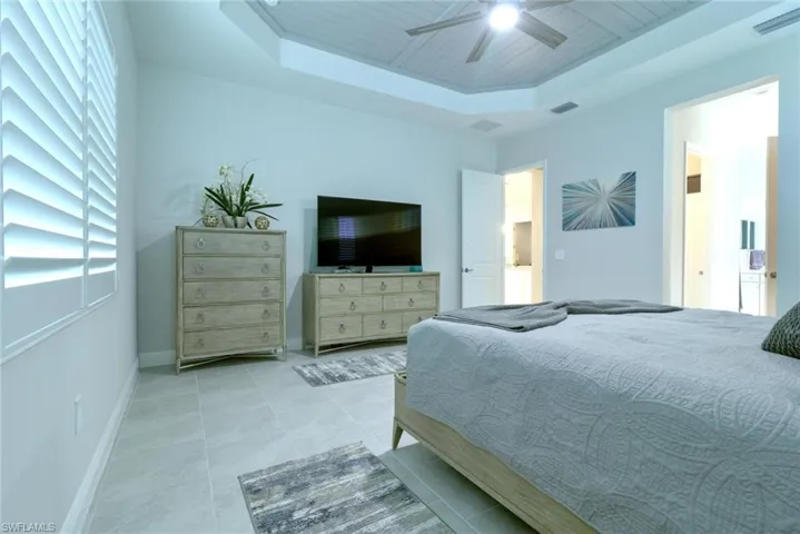 Spacious Primary bedroom with tile floors, trey ceiling with custom shiplap inlay and ceiling fan light