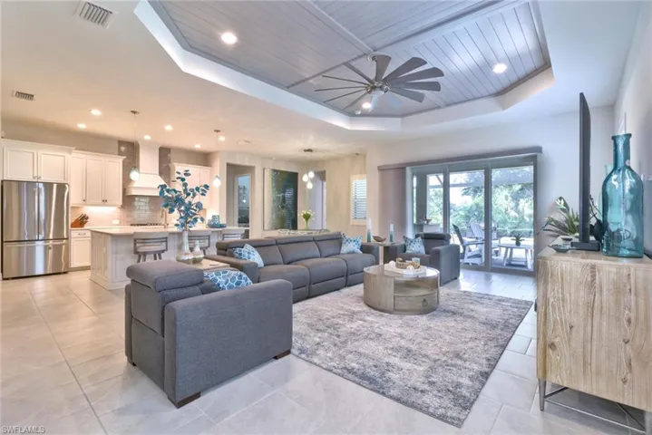 Tiled living room with ceiling fan, a raised ceiling, and wooden ceiling