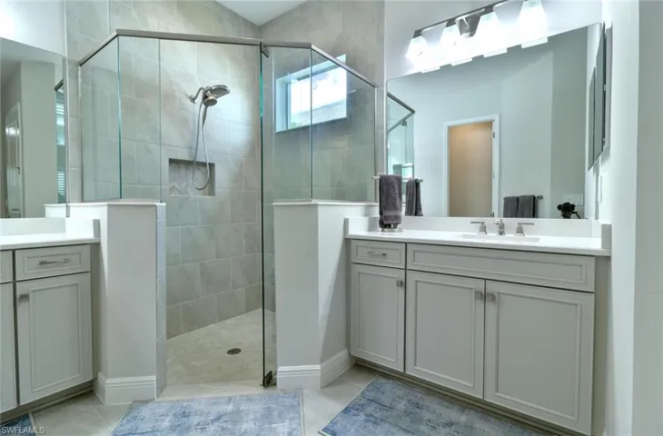 Primary bathroom featuring two vanities, walk-in shower with tile floors