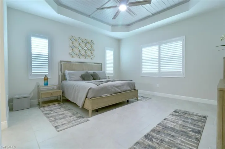 Spacious Primary bedroom with custom shiplap tray ceiling with a ceiling fan light and tile floors