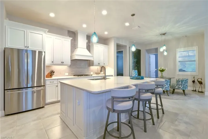 Kitchen with a kitchen island with sink, stainless steel appliances, sink, custom range hood, and white cabinets