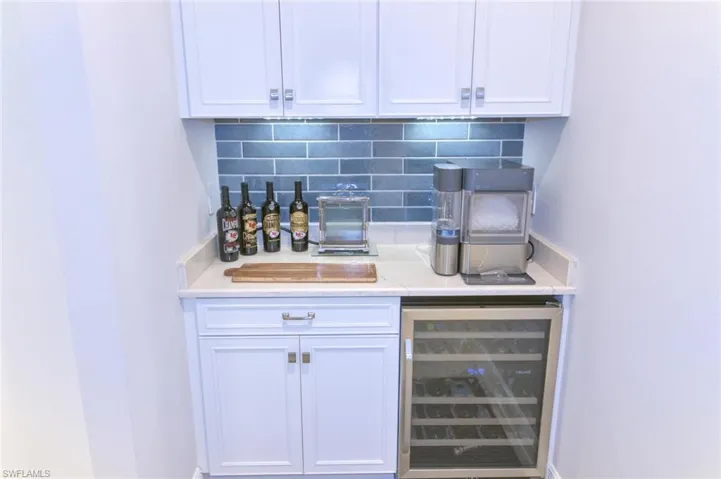 Bar featuring light stone counters, white cabinetry, decorative backsplash, and wine cooler