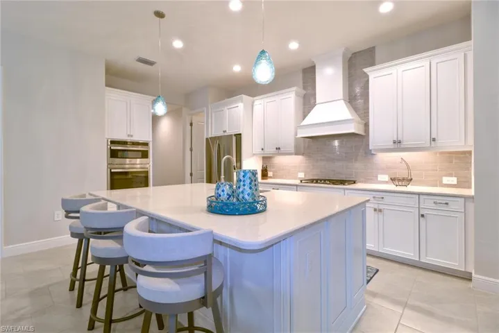 Kitchen with a kitchen bar, hood, white cabinetry, and a kitchen island with sink