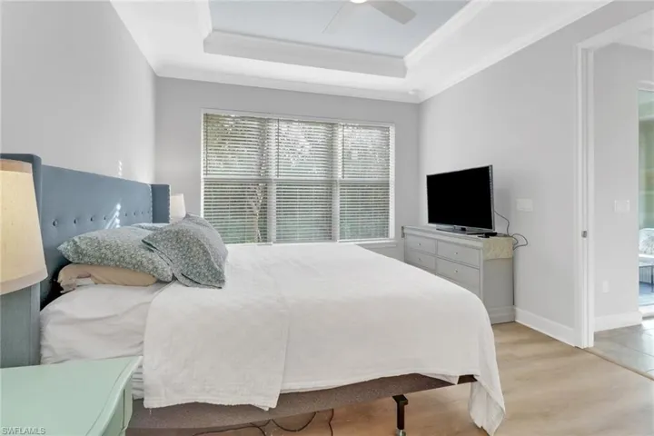 Bedroom with ceiling fan, a raised ceiling, light wood-type flooring, and crown molding
