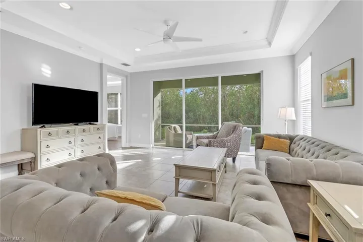 Living room featuring ceiling fan, light tile patterned flooring, crown molding, and a tray ceiling