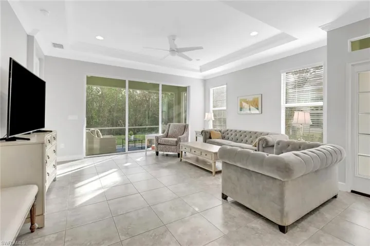 Living room featuring a tray ceiling, ceiling fan, crown molding, and light tile patterned floors