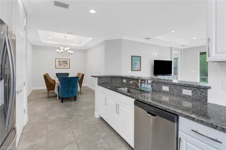 Kitchen with appliances with stainless steel finishes, a tray ceiling, sink, dark stone countertops, and white cabinetry