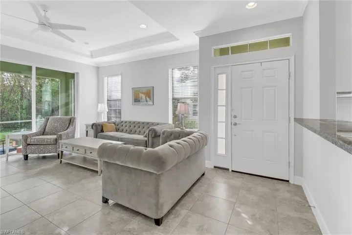 Tiled living room featuring a raised ceiling, crown molding, ceiling fan, and a healthy amount of sunlight
