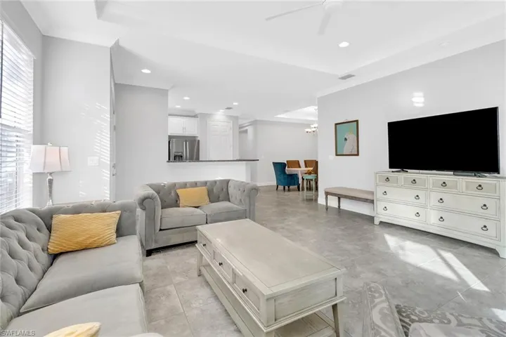 Living room with ceiling fan with notable chandelier, a tray ceiling, crown molding, and light tile patterned flooring