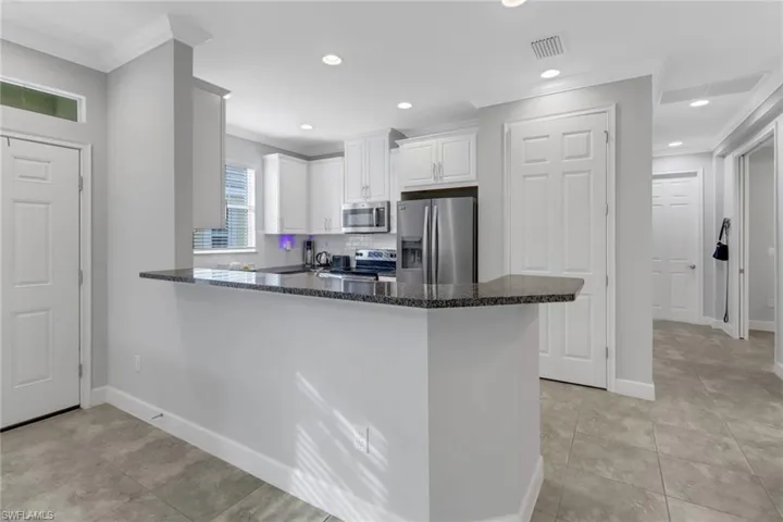 Kitchen featuring white cabinets, kitchen peninsula, ornamental molding, and appliances with stainless steel finishes