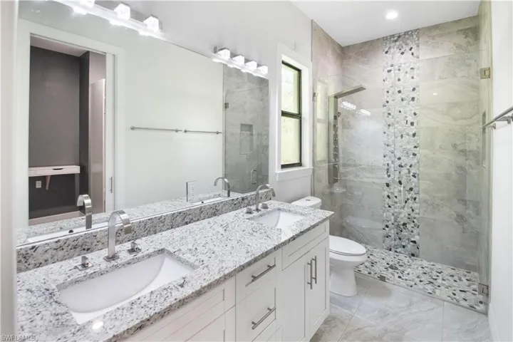 Bathroom featuring tile floors, a shower with door, toilet, and double sink vanity
