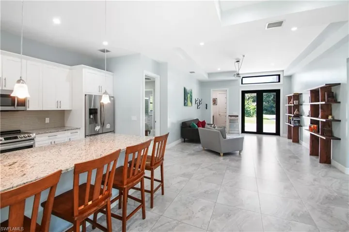 Kitchen with appliances with stainless steel finishes, a tray ceiling, a breakfast bar area, light stone counters, and tasteful backsplash