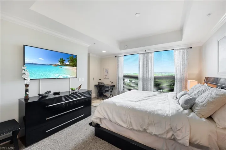 Spacious Bedroom with crown molding, light colored carpet, a desk, and a raised ceiling