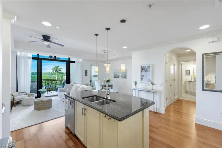 Kitchen with open floor plan, dark stone countertops, New hanging light fixtures, light wood finished floors, and arched walkways