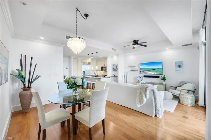 Dining space featuring ceiling fan, light wood-type flooring, recessed lighting, a tray ceiling, and a chandelier