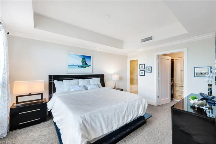Bedroom with crown molding, light colored carpet, a raised ceiling, and ensuite bathroom