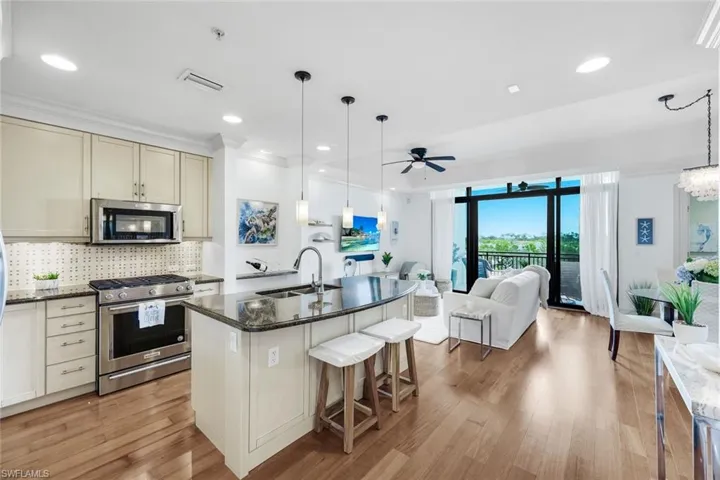 Kitchen featuring stainless steel appliances, dark stone countertops, a ceiling fan, open floor plan, and decorative light fixtures