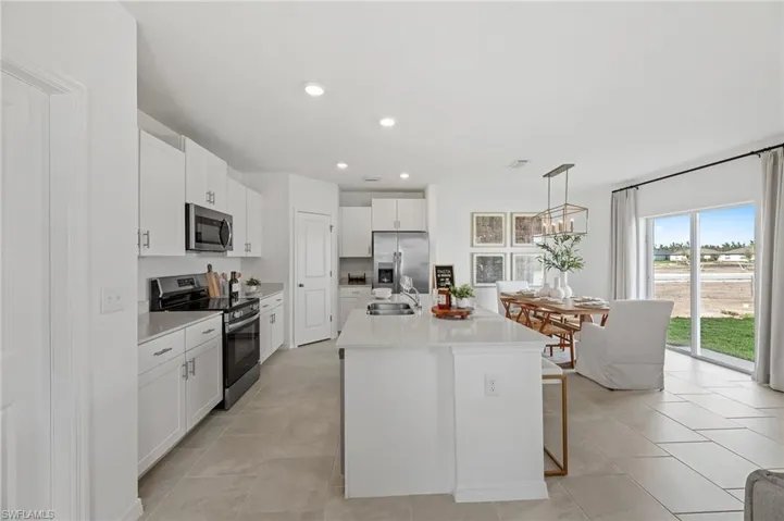 Kitchen with appliances with stainless steel finishes, white cabinetry, light countertops, an island with sink, and decorative light fixtures