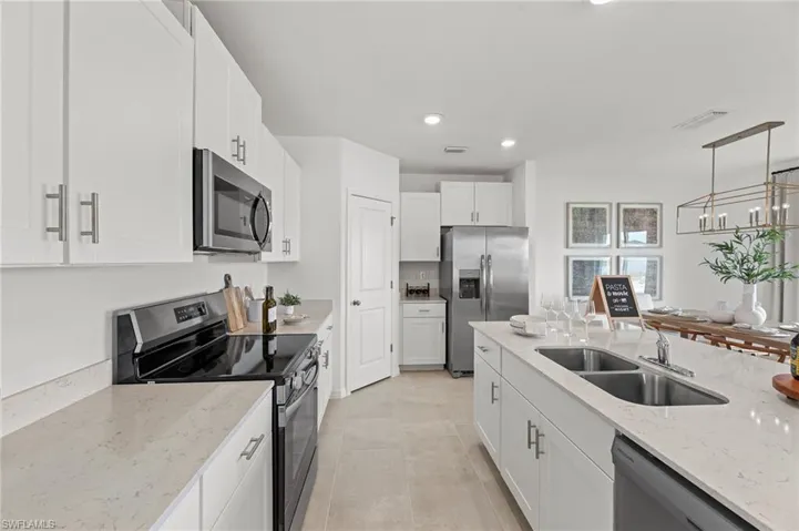 Kitchen featuring stainless steel appliances, light stone countertops, white cabinets, recessed lighting, and decorative light fixtures