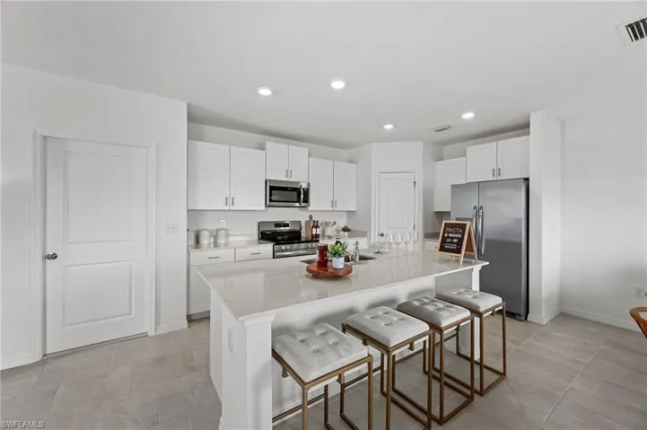 Kitchen with appliances with stainless steel finishes, a kitchen breakfast bar, white cabinetry, a center island with sink, and recessed lighting