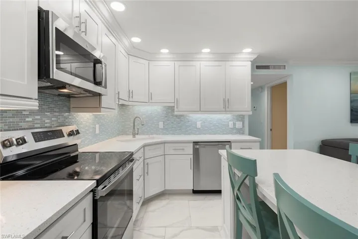 White shaker-style cabinetry, stainless steel appliances, light-toned countertops, tile backsplash, and recessed lighting