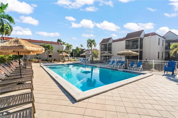 Community swimming pool with surrounding paver deck, white perimeter fencing, and established palm trees