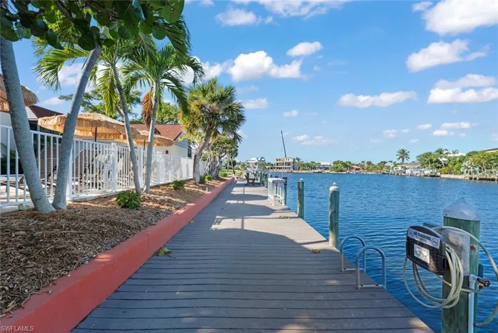 Waterfront property featuring a wooden dock, multiple boat slips, and mature palm trees