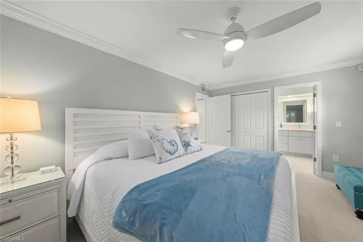Crown molding, ceiling fan with integrated lighting, built-in closet with bi-fold doors, plush carpeting, and an adjoining room with a vanity
