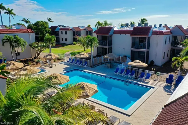 Community swimming pool with surrounding paver deck, multiple thatched umbrellas, and lounge seating