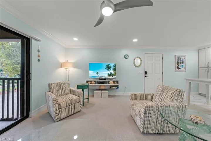 Sliding glass patio door with black frame, recessed lighting, ceiling fan with light, crown molding, and white built-in cabinetry