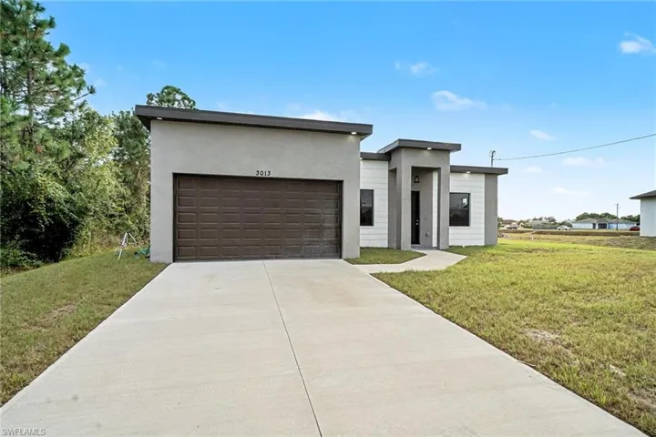 Contemporary home featuring stucco siding, a front yard, concrete driveway, and an attached garage