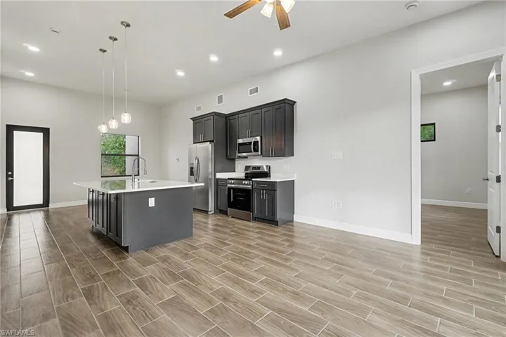 Kitchen featuring appliances with stainless steel finishes, a center island with sink, decorative light fixtures, recessed lighting, and wood tiled floors