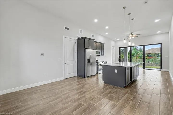 Kitchen with hanging light fixtures, a kitchen island with sink, ceiling fan, light stone counters, and wood finish floors