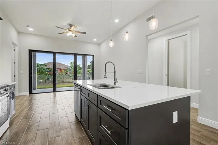 Kitchen with hanging light fixtures, wood finish floors, ceiling fan, a kitchen island with sink, and appliances with stainless steel finishes