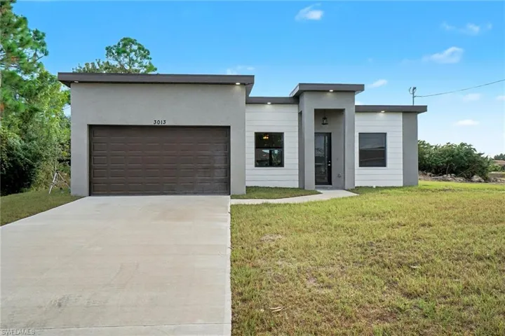 Modern home featuring driveway, an attached garage, a front yard, and stucco siding