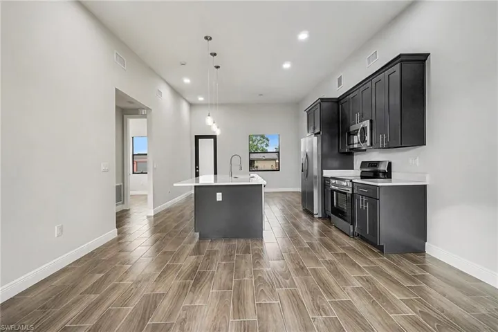 Kitchen featuring an island with sink, stainless steel appliances, dark cabinets, decorative light fixtures, and recessed lighting