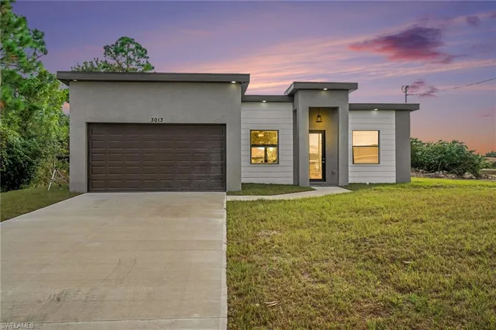 Contemporary house featuring driveway, an attached garage, a yard, and stucco siding
