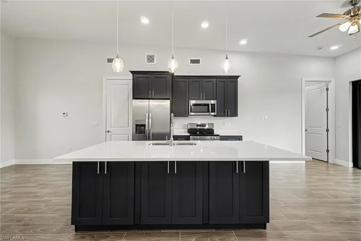 Kitchen with dark cabinetry, stainless steel appliances, an island with sink, light stone countertops, and a kitchen bar