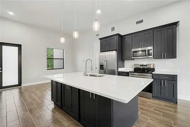 Kitchen with dark cabinetry, wood tiled floors, stainless steel appliances, pendant lighting, and light stone counters