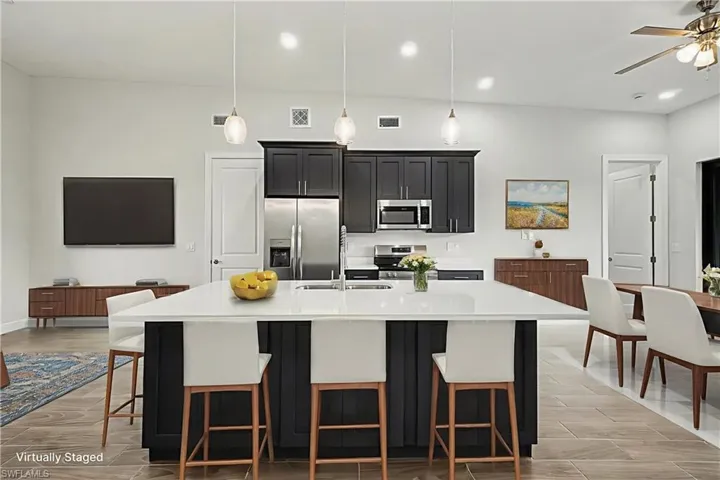 Kitchen featuring dark cabinetry, a kitchen breakfast bar, stainless steel appliances, an island with sink, and light stone countertops