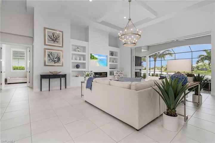 Living room featuring beamed ceiling, a high ceiling, built in features, a glass covered fireplace, and a baseboard radiator