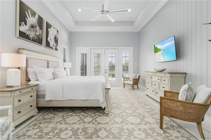 Tiled bedroom featuring access to exterior, a tray ceiling, a ceiling fan, french doors, and wooden walls