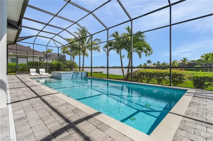 View of swimming pool featuring a water view, a pool with connected hot tub, a patio area, and glass enclosure