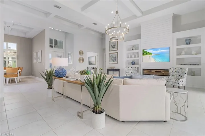 Living area featuring a chandelier, beamed ceiling, light tile patterned floors, built in features, and a towering ceiling