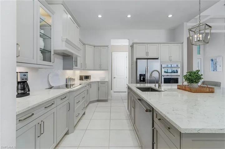 Kitchen with a spacious island, appliances with stainless steel finishes, recessed lighting, hanging light fixtures, and glass insert cabinets