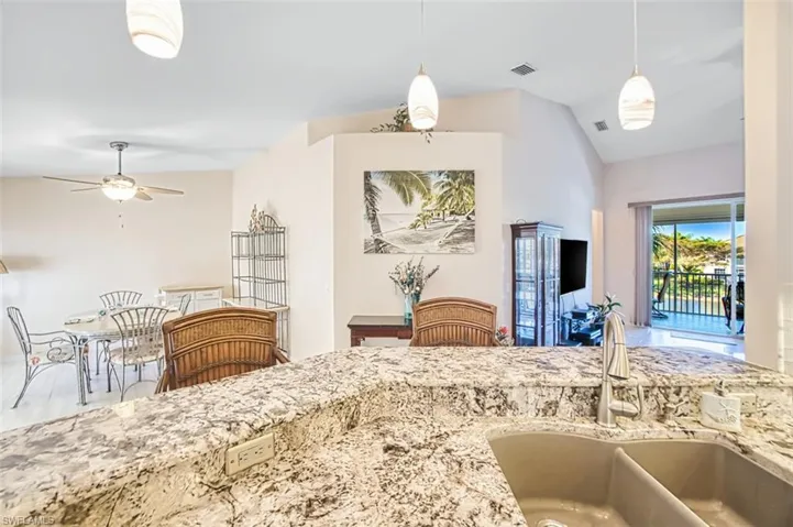 Kitchen featuring a ceiling fan, vaulted ceiling, light stone counters, and pendant lighting
